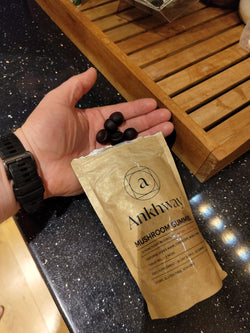 A hand holding black mushroom gummies with an Ankhway Mushroom Gummies packet on a countertop.