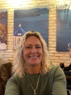 A smiling person taking a selfie in a room with scenic posters on the wall.